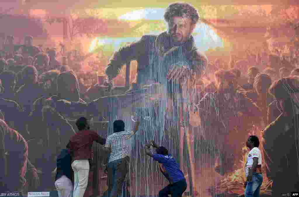 Indian fans spray milk on a billboard displaying the picture of Bollywood star Rajinikanth in a celebratory gesture intended to bless their favorite film star's new movie, before attending the show of the new Tamil-language film 'Pettai' in Chennai, Jan. 10, 2019.