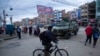 Un hombre con una máscara facial protectora contra la propagación del nuevo coronavirus, pasa su bicicleta frente a un vehículo blindado militar que patrulla las calles durante una cuarentena en El Alto, Bolivia, el viernes 20 de marzo de 2020. 