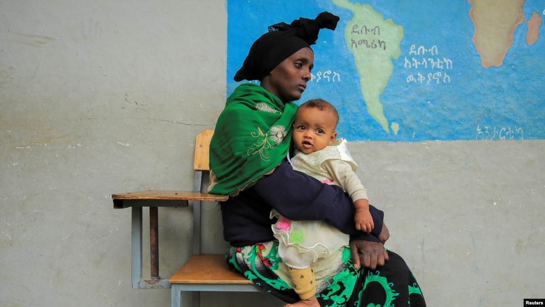 FILE - Habtam Akele carries her daughter as they sit at a school makeshift camp for internally displaced people due to the fighting between the Ethiopian National Defense Force and the Tigray People's Liberation Front forces, in Dessie, Amhara Region, Ethiopia, Oct. 9, 2021.