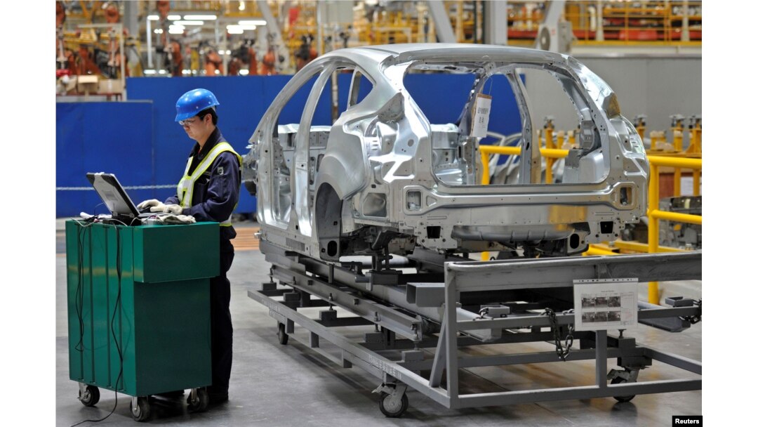 FILE - An employee uses a laptop next to a car body at an assembly line at a Ford manufacturing plant in Chongqing municipality, April 20, 2012.