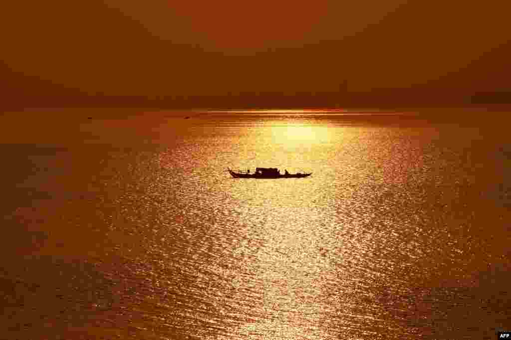A fishing boat travels along the Mekong River as sunrises over Phnom Penh.