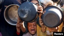 Palestinianos reúnem-se para receber alimentos confeccionados por uma cozinha de caridade, no meio de uma crise de fome, em Khan Younis