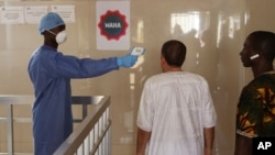 A health worker, center, takes the temperature of people to see if they might be infected by the Ebola virus inside the Ignace Deen government hospital in Conakry, Guinea, March 18, 2016.