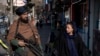 ARCHIVO - Un combatiente talibán monta guardia mientras una mujer pasa caminando en Kabul, Afganistán, el 26 de diciembre de 2022. 