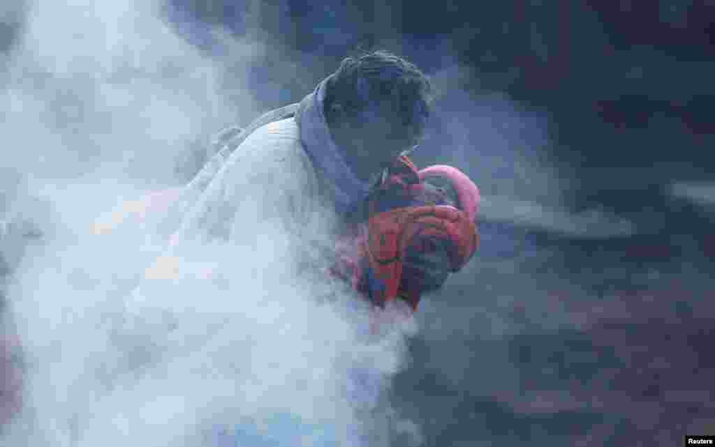 A man holding a baby wrapped in a blanket stands next to a bonfire on a cold winter morning in New Delhi, India.