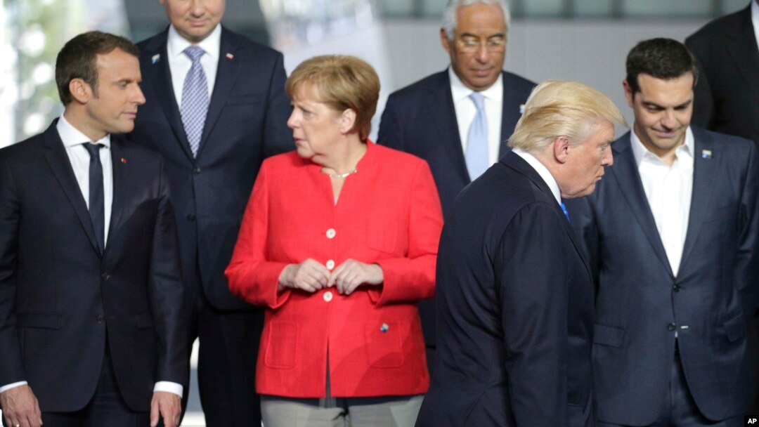 File - French President Emmanuel Macron, left, speaks with German Chancellor Angela Merkel, second left, as President Trump takes his position during a group photo at the new NATO headquarters in Brussels on Thursday, May 25, 2017. 