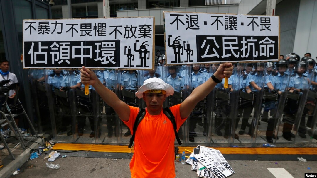 A protester holds up placards which reads "Occupy Central" (L) and "Civil Disobedience" in front of a line of riot police outside government headquarters in Hong Kong, Sept. 27, 2014. 