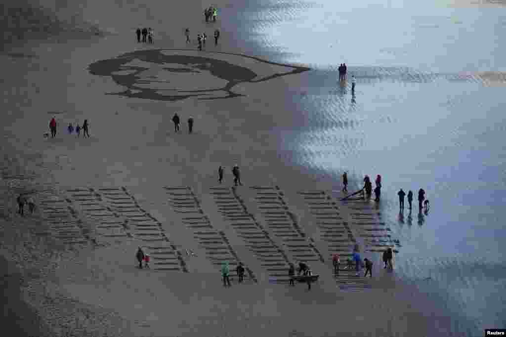 People gather to look at an Armistice day sand portrait of Imperial Military Nurse Rachel Ferguson who died in June 1918 during World War I, created as part of Danny Boyle's Pages of The Sea celebrations, on Downhill Beach in Coleraine, Northern Ireland.