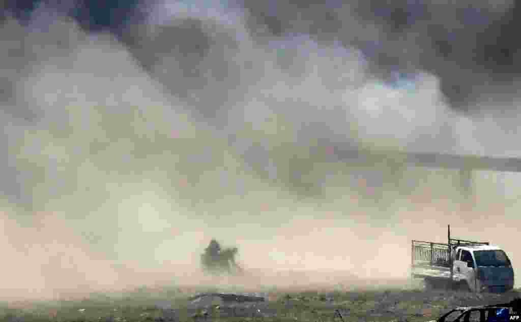 People are seen fleeing as heavy smoke rises above the Islamic State (IS) group's last remaining position in the village of Baghouz during battles with the Syrian Democratic Forces (SDF), in the countryside of the eastern Syrian province of Deir Ezzor.
