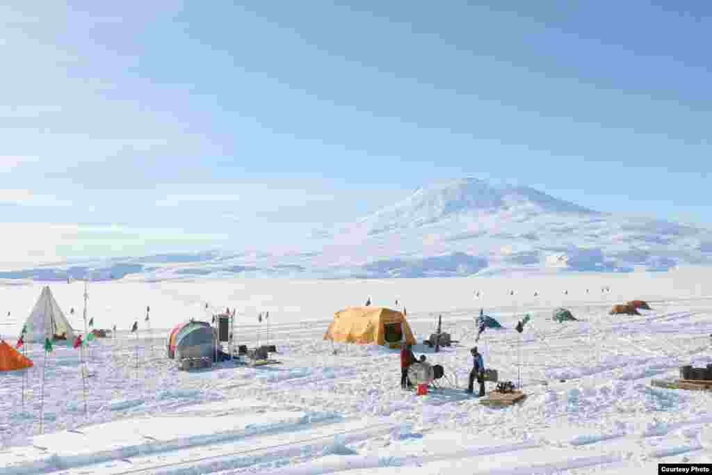 Nine hundred meters of fiber cable are being lowered to the ocean below (center right) through a just-completed borehole. A second borehole is just being started in the white drilling tent (far left). (Victor Zagorodnov)