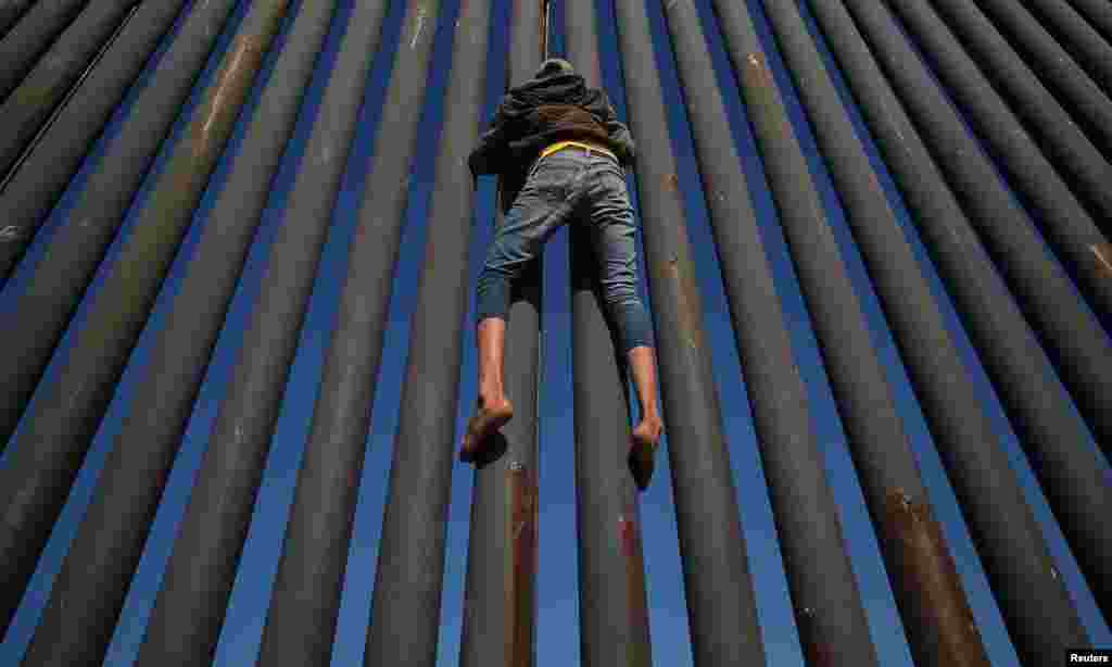 A migrant, part of a caravan of thousands from Central America trying to reach the United States, climbs the border fence between Mexico and the United States, in Tijuana, Mexico, Nov. 18, 2018.