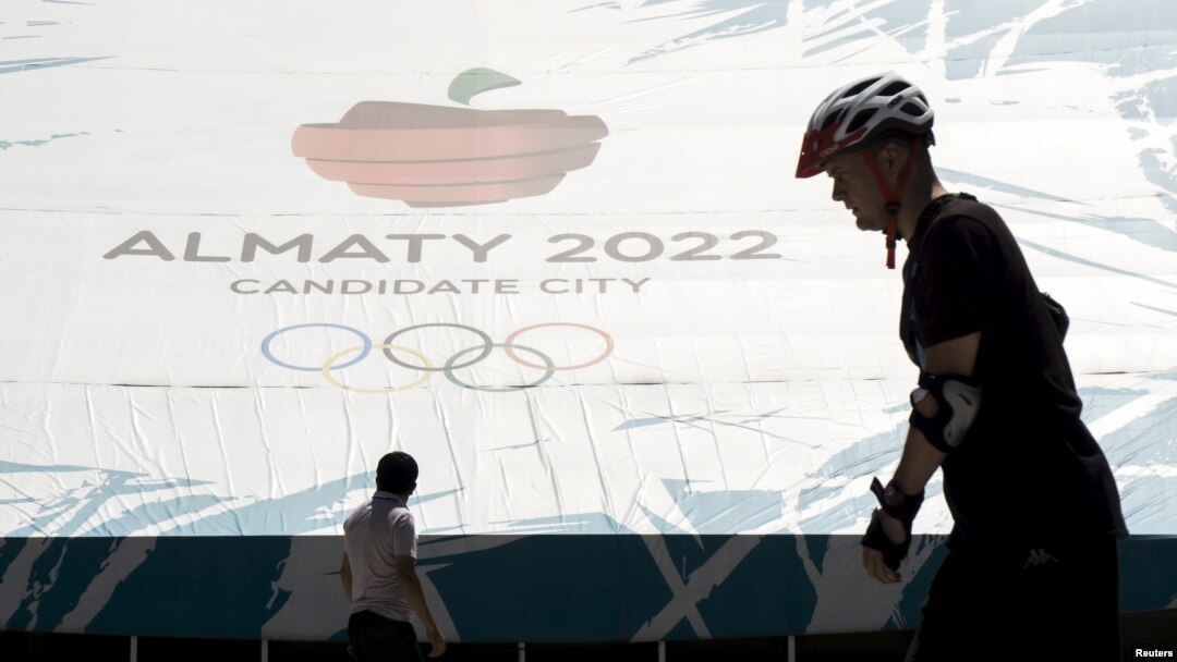 People walk past a banner promoting Almaty candidate city for 2022 Winter Olympic Games at the Medeu skating oval in Almaty, Kazakhstan, July 26, 2015.