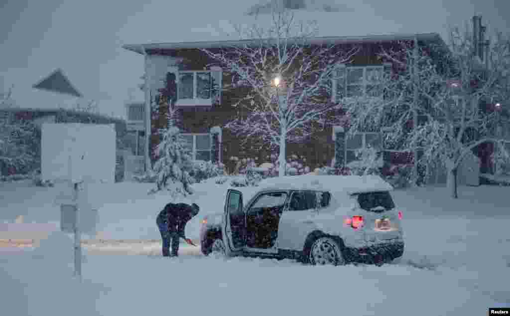 A woman shovels snow around her stuck car during a snowstorm in Arlington Heights, Illinois.