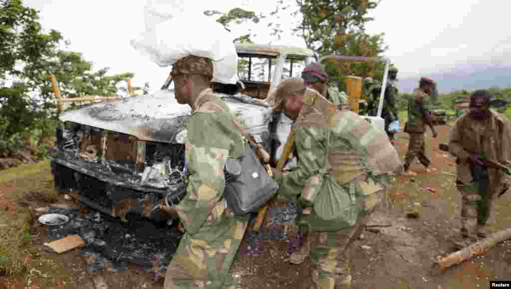 Congolese soldiers carry weapons as they walk near a damaged vehicle after the surrender of M23 rebel fighters in Chanzo village near the eastern town of Goma, Nov. 5, 2013.