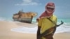 FILE - A masked and armed Somali pirate stands near a fishing vessel.