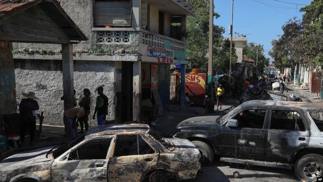 Los residentes pasan junto a vehículos incendiados por bandas armadas en el barrio de Poste Marchand de Puerto Príncipe, Haití, el martes 10 de diciembre de 2024. 