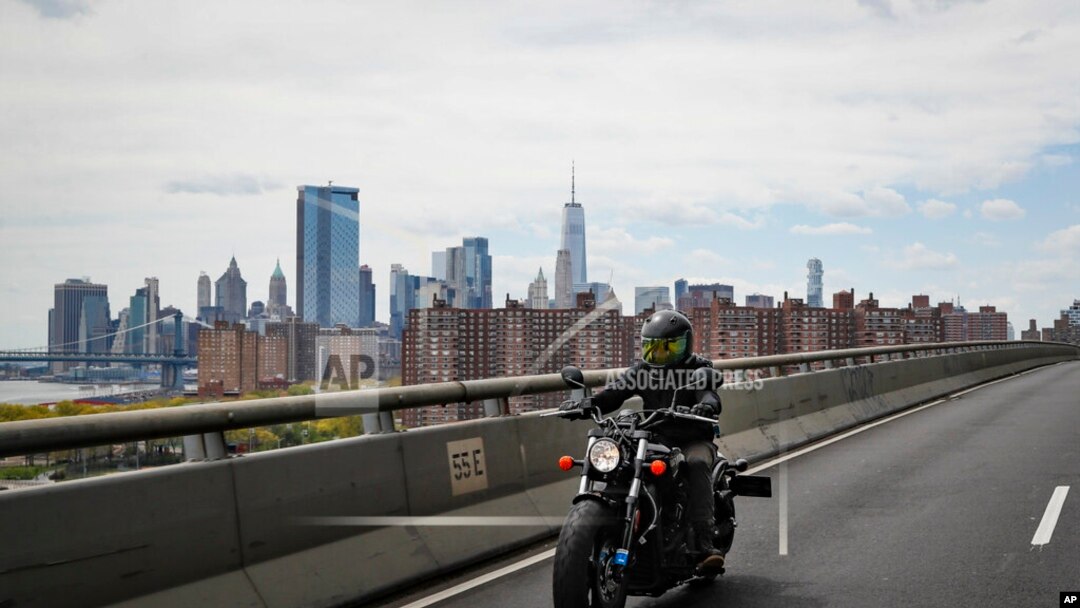 Ashley Zeolla rides her motorcycle over the Williamsburg Bridge on a delivery run of personal protective equipment to a doctors office with Masks for Docs as the lower Manhattan skyline looms in the distance, May 3, 2020, in New York. 