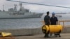 A U.S. naval officer talks with a crewman as they stand next to part of the towed pinger locator before its fitted to the defense ship Ocean Shield to aid in her roll in the search for missing Malaysia Airlines Flight MH370 in Perth, Australia, Sunday, Ma