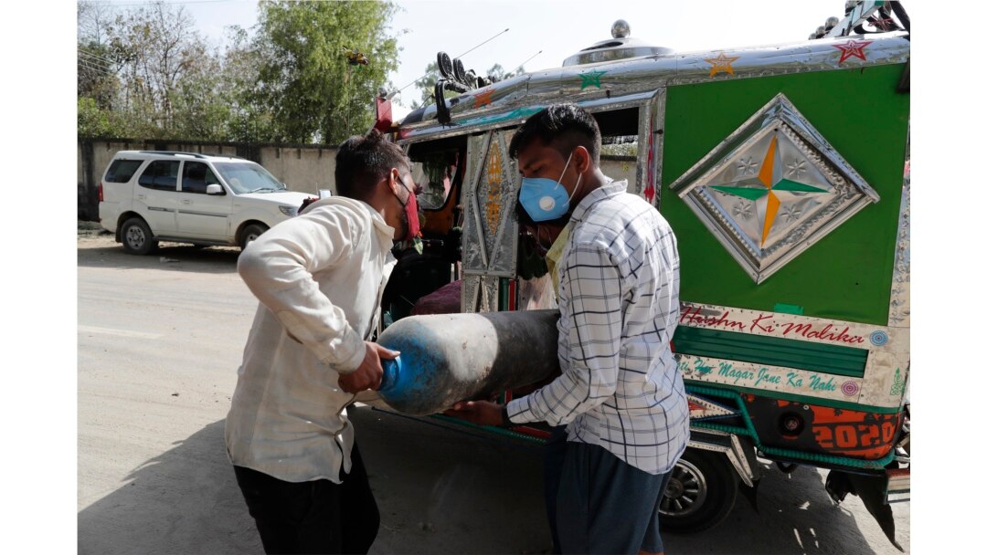 People carry a medical oxygen cylinder at a charging station on the outskirts of Prayagraj, India, Friday, April 23, 2021. I
