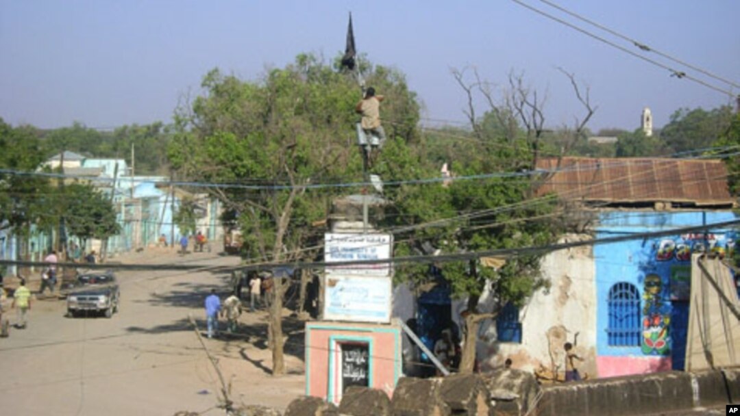 A man climbs onto a Somali university building to take down an Al-Shabab flag in the center of Baidoa, a day after the town was seized by Ethiopian troops and allied Somali government forces on February 23, 2012.