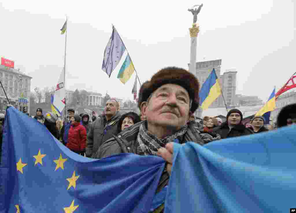 A pro-European Union activist with Ukrainian and European Union flags stands with others in Independence Square in Kyiv, Ukraine.