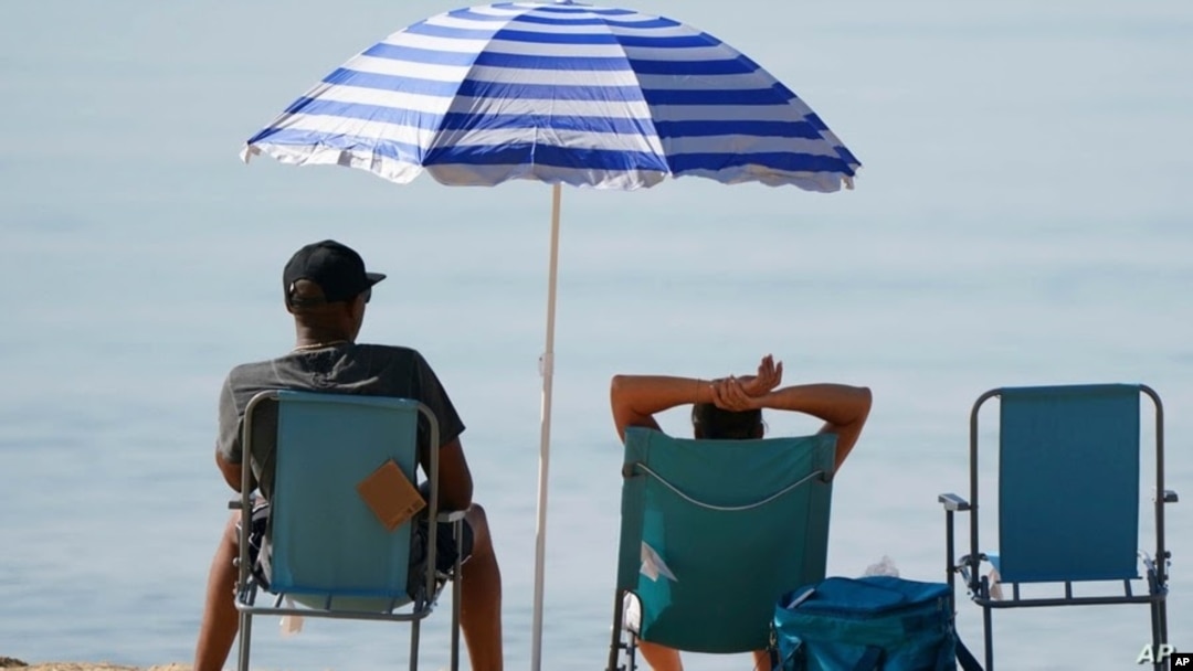 Vacacionistas se relajan bajo una sombrilla en la playa durante una calurosa mañana en Bournemouth, sur de Inglaterra, el 20 de julio de 2021.