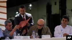 Alias 'Pablo Beltrán', de la guerrilla del ELN, recibe documentos para firmar junto al miembro del grupo, Antonio García, en el centro, mientras se sientan con el representante del gobierno colombiano Iván Danilo Rueda en Caracas, Venezuela, el 4 de octubre de 2022.