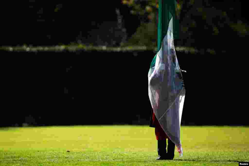 A military cadet is silhouetted while holding a Mexican flag during a troop review by Mexico's new President Andres Manuel Lopez Obrador at Campo Marte, Mexico City, Dec. 2, 2018.