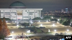 Pessoas frente à Assembleia Nacional em Seul, a 4 de dezembro de 2024, depois de o Presidente da Coreia do Sul, Yoon Suk Yeol, ter declarado a lei marcial.
