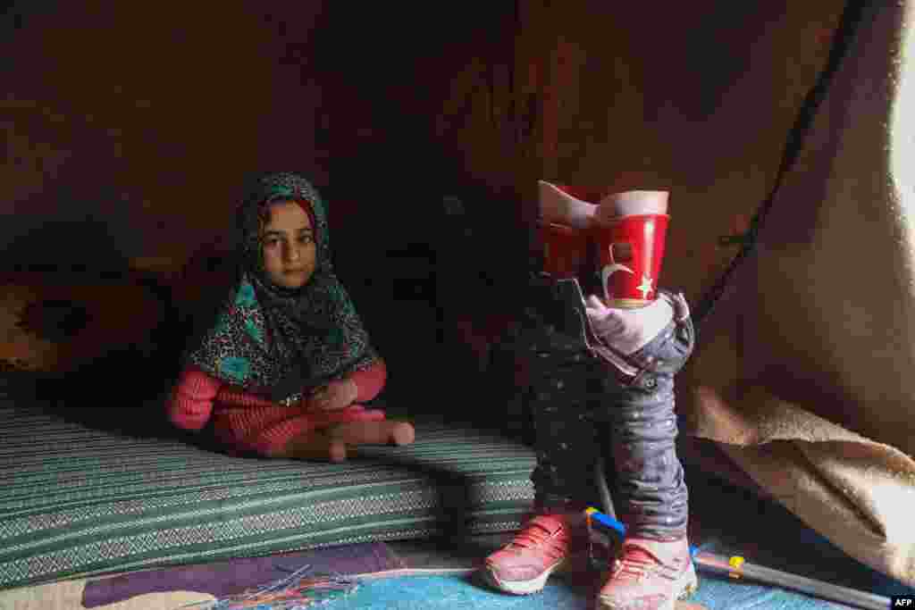 Maya Merhi, 8, from Syria, poses for a picture next to her prosthetic legs that are decorated with the Turkish flag inside a tent at the Internally Displaced Persons (IDP) camp of Serjilla in northwestern Syria, next to Bab al-Hawa border crossing with Turkey. Maya, born with no legs due to a congenital condition, had to struggle around the camp on artificial limbs made of plastic tubing and tin cans. Today, she can walk with her new prosthetics after undergoing treatment in Turkey.