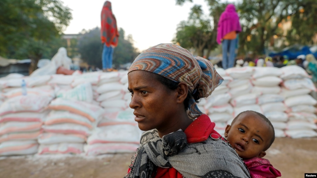 A woman carries an infant as she queues in line for food, at the Tsehaye primary school, which was turned into a temporary shelter for people displaced by conflict, in the town of Shire, Tigray region, Ethiopia, March 15, 2021.
