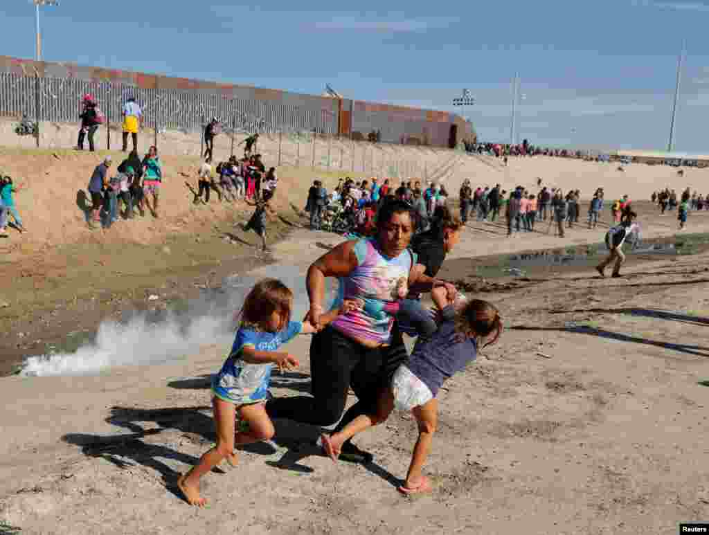 A migrant family, part of a caravan of thousands traveling from Central America en route to the United States, run away from tear gas in front of the border wall between the U.S and Mexico in Tijuana, Mexico, Nov. 25, 2018. U.S. authorities shut the country's busiest border crossing and fired tear gas into Mexico to repel Central American migrants approaching the border.