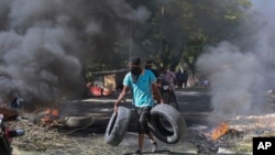 Haitiano carrega pneus para serem colocados numa barricada em chamas para impedir que membros de gangues entrem no seu bairro, em Porto Príncipe, Haiti, a 19 de novembro de 2024.