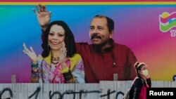 Una mujer con un cubreboca pasa por delante de una valla que data de marzo de 2020 en la que parecen las imágenes del presidente Daniel Ortega y su esposa Rosario Murillo en Managua, Nicaragua.