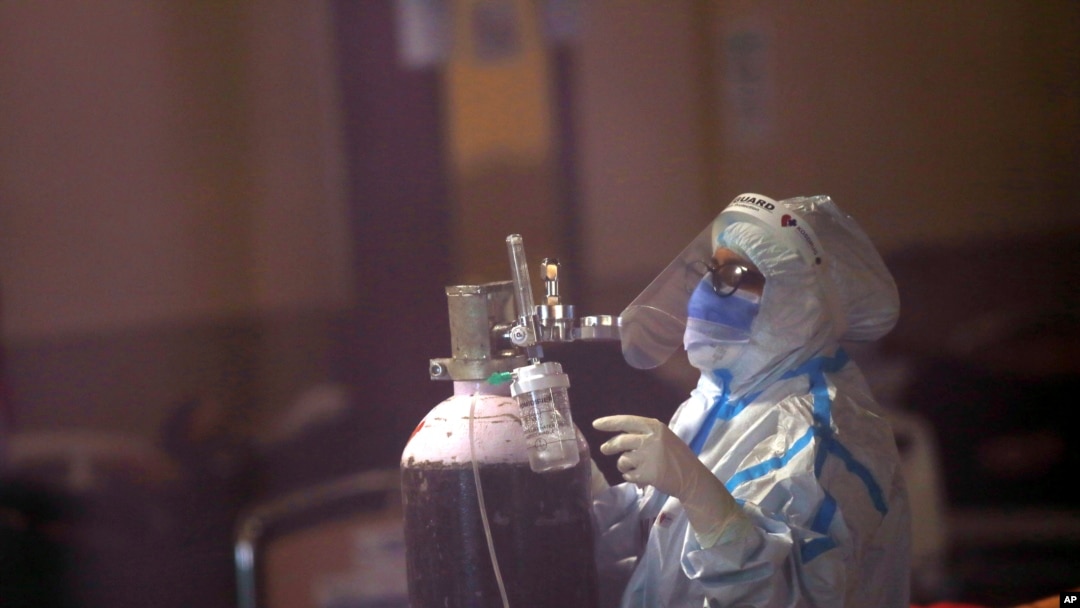 A health worker fixes an oxygen cylinder for a COVID-19 patient at a banquet hall converted into a quarantine center ,in New Delhi, India, Friday, April 23, 2021.