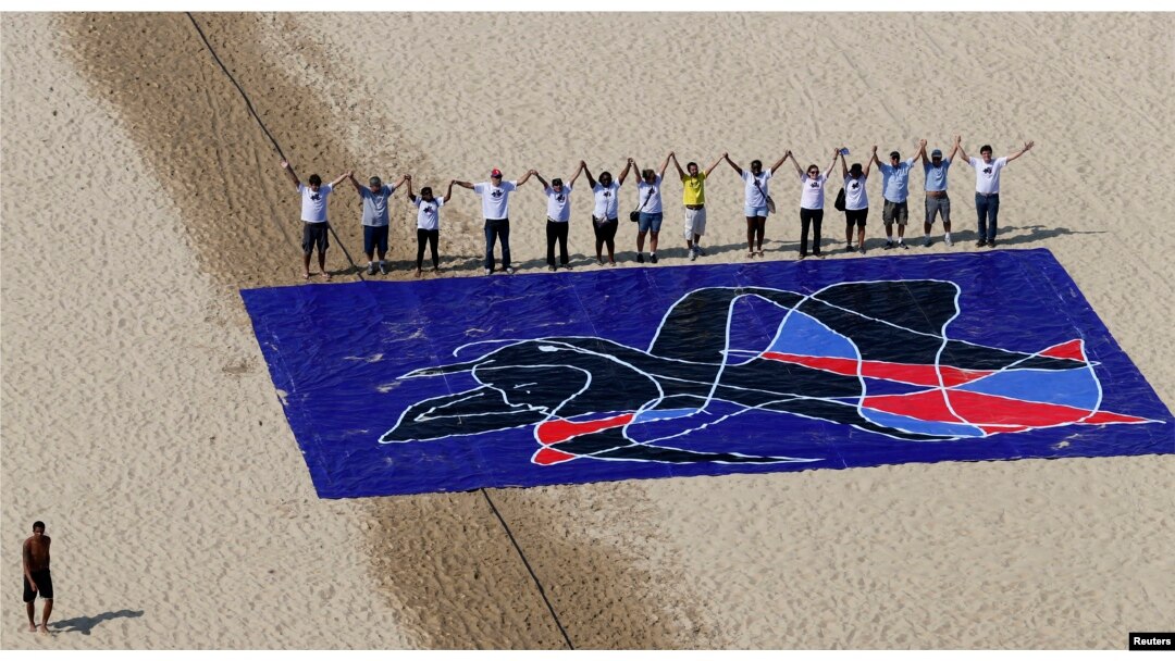 FILE - People from the Baha'i religious community pose for a picture next to a giant painting created by Brazilian artist Siron Franco, as part of the "Five Years Too Many" protest campaign marking the five-year anniversary of the imprisonment of seven Iranian Baha'i leaders, on Copacabana Beach in Rio de Janeiro, May 5, 2013.