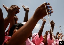 FILE - Women from a Catholic society wave rosary beads as they watch the convoy of Pope Benedict XVI pass on the way to a meeting between the pope and Cameroonian bishops, in Yaounde, March 18, 2009.