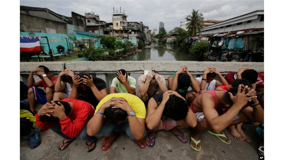 FILE - Filipino men place their hands over their heads as they are rounded up during a police operation as part of the continuing "War on Drugs" campaign of Philippine President Rodrigo Duterte in Manila, Philippines.
