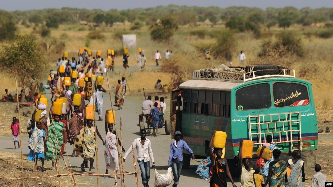 Internally displaced people carry water from outside as they walk toward the entrance of a United Nations Mission in the Republic of South Sudan base in Malakal, Feb. 6, 2014.