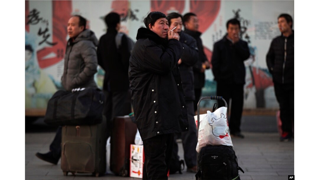 A migrant worker smokes as others wait for their trains at the Beijing railway station in Beijing, Monday, Jan. 21, 2019. China's economic growth hit a three-decade low in 2018.