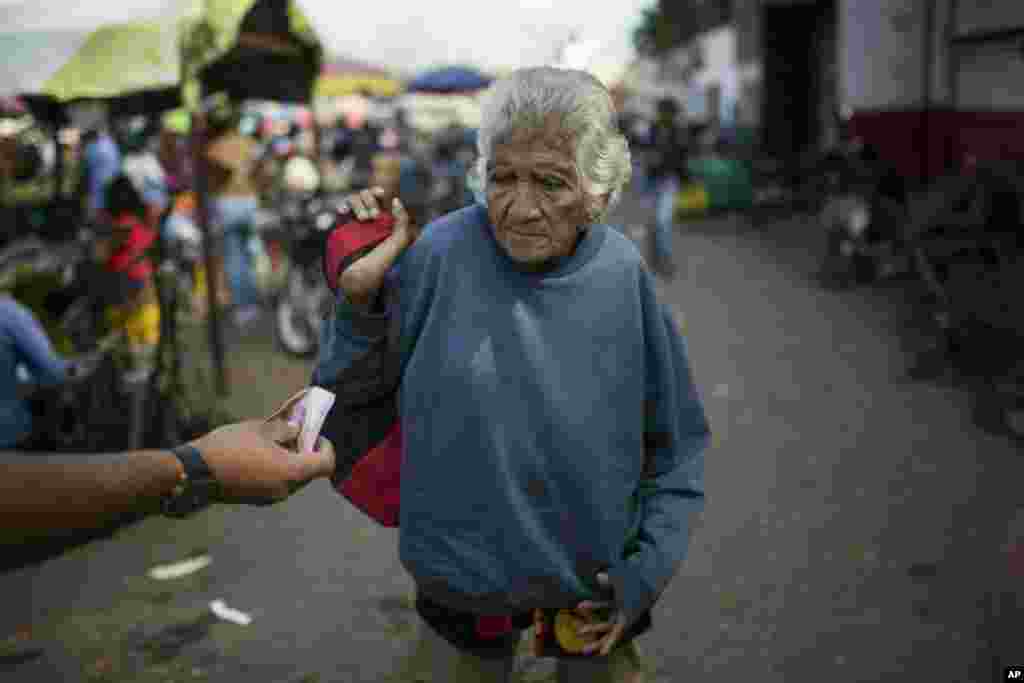 An elderly woman is offered cash at a wholesale food market in Caracas, Venezuela.