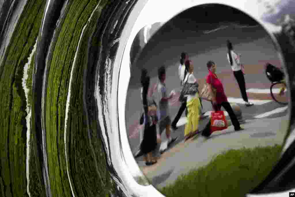 Pedestrian and plants on a sidewalk are reflected on a sculpture on display outside a commercial building in Beijing, China.