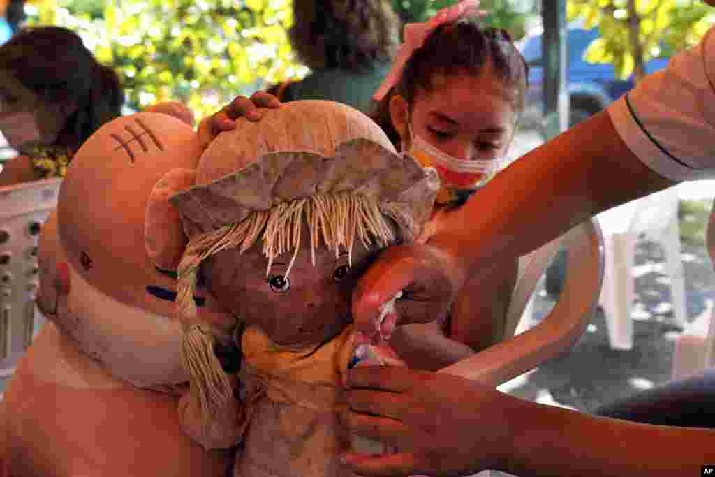 A health worker pretends to give a shot to a girl's doll to help put her at ease before giving her a shot of COVID-19 vaccine, at a sports center as children start getting vaccinated in Asuncion, Paraguay.