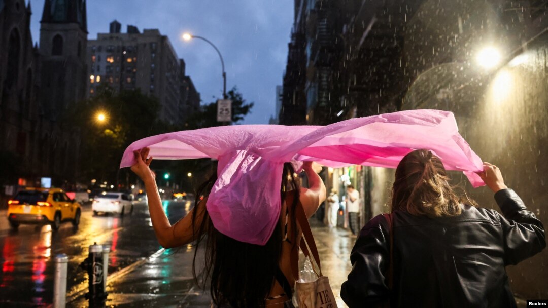 People shield themselves with a plastic rain poncho during a rainstorm in New York City, Aug. 6, 2024. 