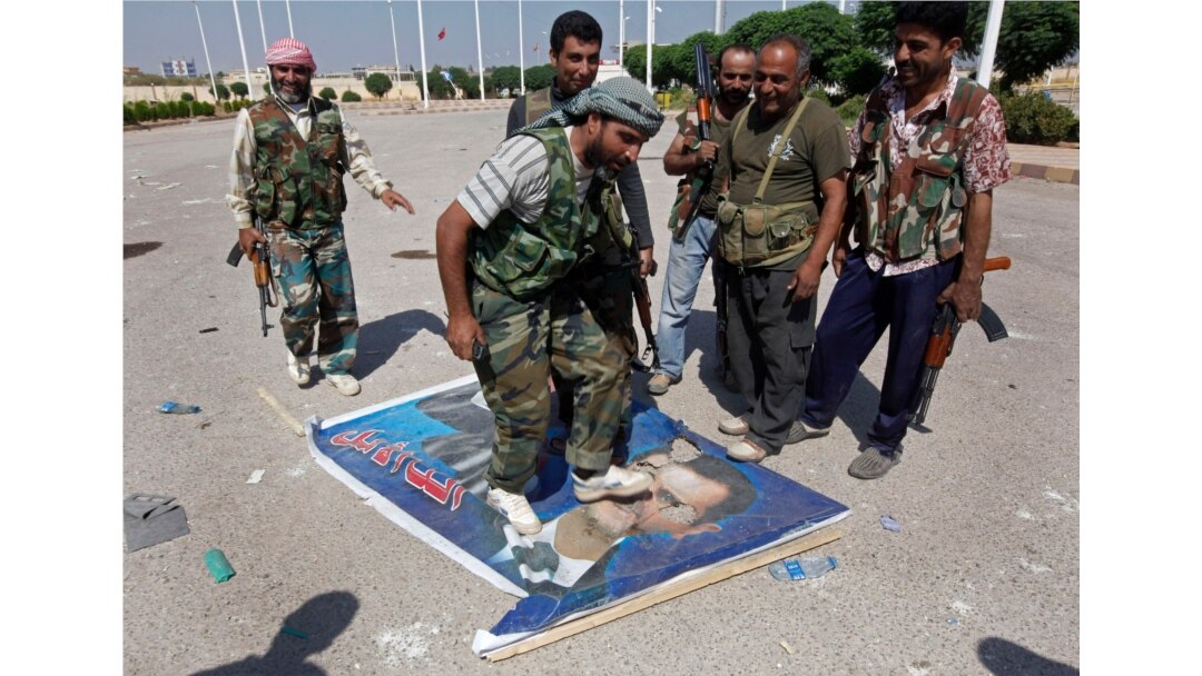 FILE - A Free Syrian Army fighter, center, steps on a poster depicting Syrian President Bashar al-Assad, at Tal Abyad, a Turkish-Syrian border crossing captured by the rebels, in eastern Syria, Sept. 22, 2012.