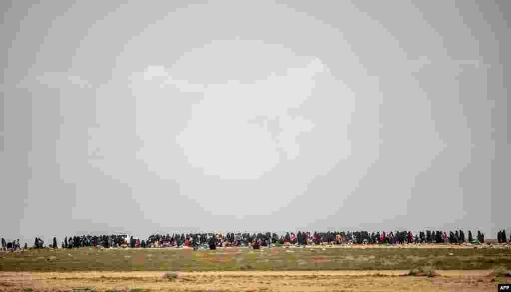 Women and children wait in a field after fleeing the Islamic State (IS) group's last holdout of Baghouz in Syria's northern Deir Ezzor province.