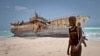 FILE - A masked Somali pirate stands near a Taiwanese fishing vessel that washed up on shore after the pirates were paid a ransom and released the crew, in the once-bustling pirate den of Hobyo, Somalia, Sept. 23, 2012. 