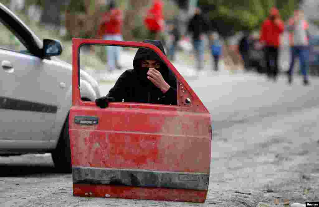 A Palestinian demonstrator takes a cover behind a car door during a protest against Jewish settlements, in Burqa village, in the Israeli-occupied West Bank.