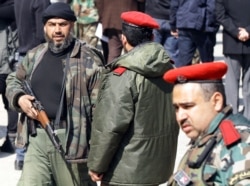 A rebel fighter, left, walks past Syrian National Defense Forces (NDF), an armed unit of volunteers loyal to President Bashar al-Assad operating under Syrian army command, in the town of Babbila, Feb. 17, 2014.
