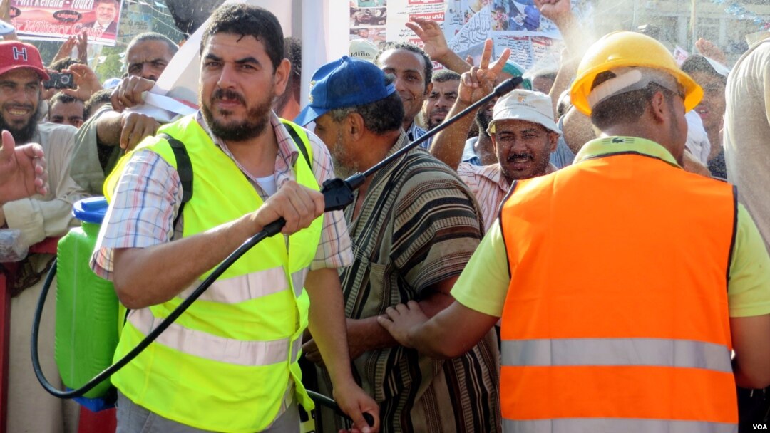 Men spray the hot crowds with cold water from plastic water packs and bottles. Currently fasting for the holy month of Ramadan, no one in this crowd takes a drink. (Heather Murdock for VOA)